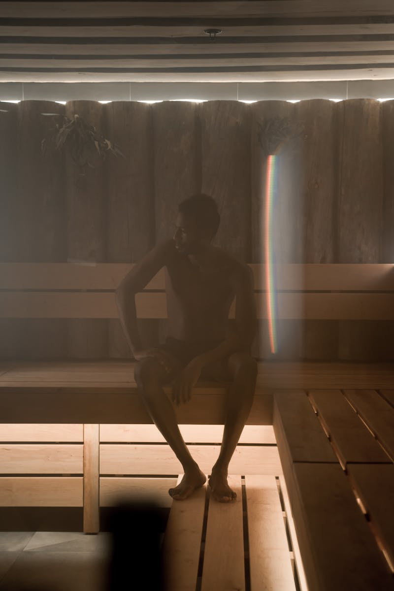 A man sitting shirtless in a dimly lit wooden sauna, creating a tranquil and calming atmosphere.